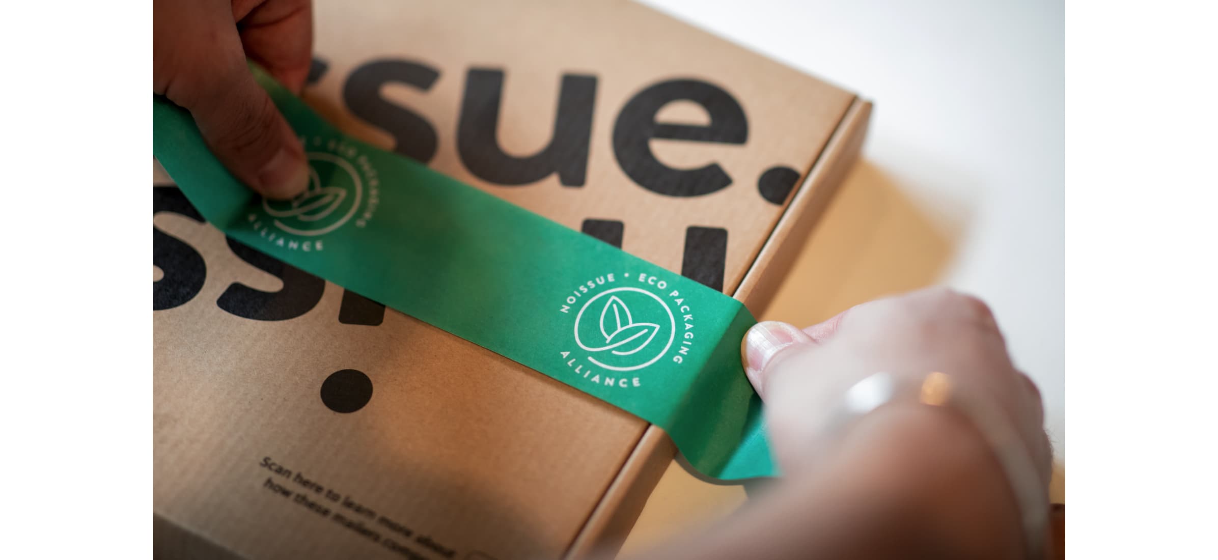 A segment of compostable tape being used to seal a cardboard box.